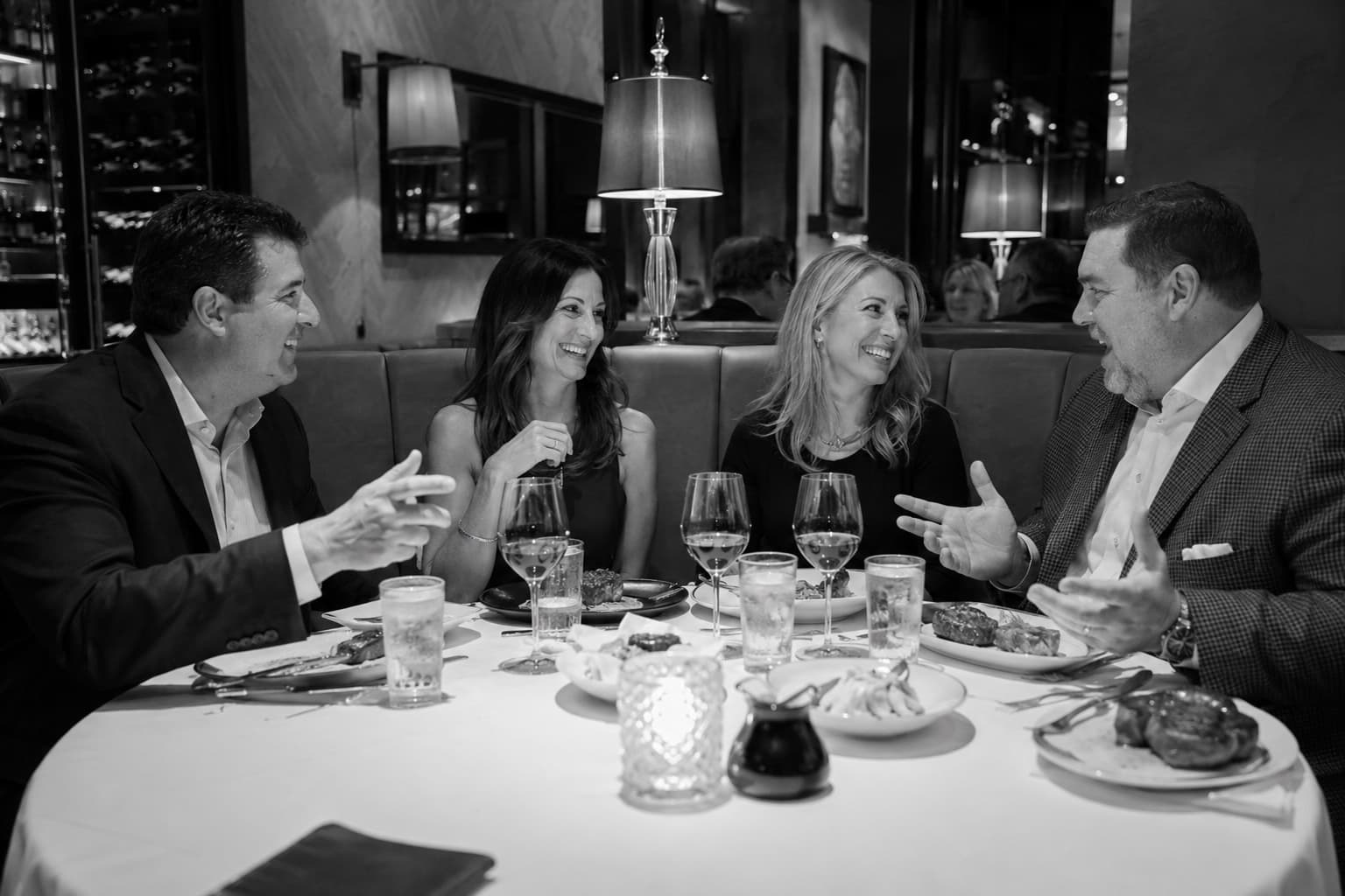 Four people at a candlelit dinner table, laughing together, black and white
